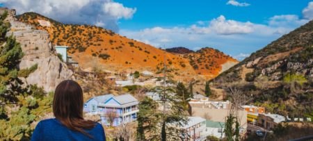 Woman in blue shirt lookingout over the buildings of a town in a valley between rocky mountain ranges