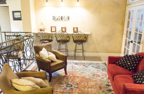 Lobby of a hotel with red couch, two tan sitting chairs and bar table with three chairs