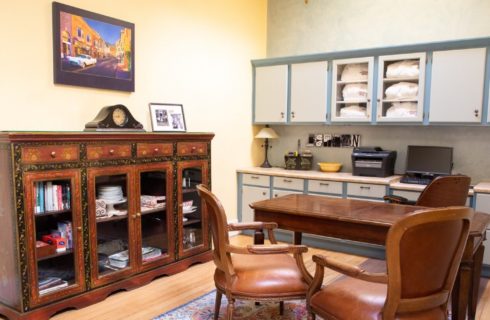 Business center with counter and cupboards, desk with three chairs and brown glass front armoire