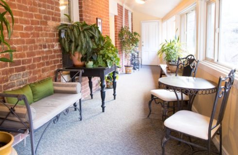 Sunroom with a wall of bright windows and iron sitting furniture in front of brick wall with several green plants