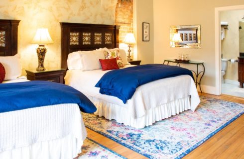 Two queen beds with white and blue bedding and brown headboards with doorway into elegant bathroom