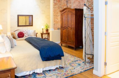 Spacious suite with bed, sitting area, large brown armoire and doorway into bathroom