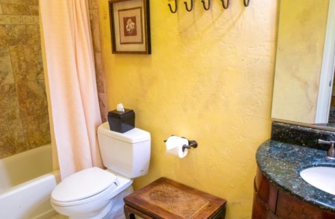 Bathroom with cream walls, tiled shower with tub, toilet, dark brown vanity and mirror