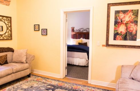 Sitting room with two tan couches with doorway into bedroom with queen bed