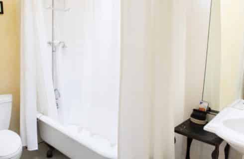 Bathroom with white clawfoot tub, white shower curtain, toilet and pedestal sink