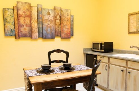 Small kitchenette with single counter and sink, table for two and artwork on yellow walls