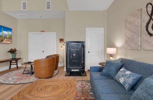 living room with hardwood floors and throw rugs, blue couch under music art, black safe, leather chairs in front of flat screened tv on wall