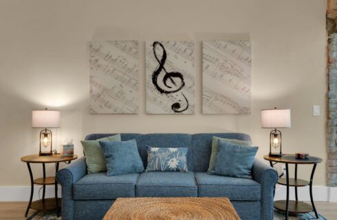 cream painted living room with blue couch with throw pillows under musical artwork, stands with lamps