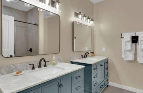 two blue vanities with marble sinks with bronze fixtures underneath rectangular mirrors, towel rack with white towels hanging
