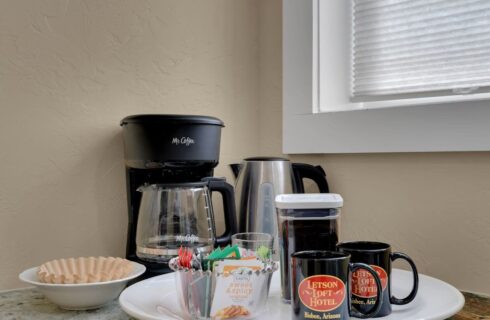 marble topped shelf holding mr coffee maker, filters in white bowl, tray with tea bags, coffee and mugs with letson loft hotel logo
