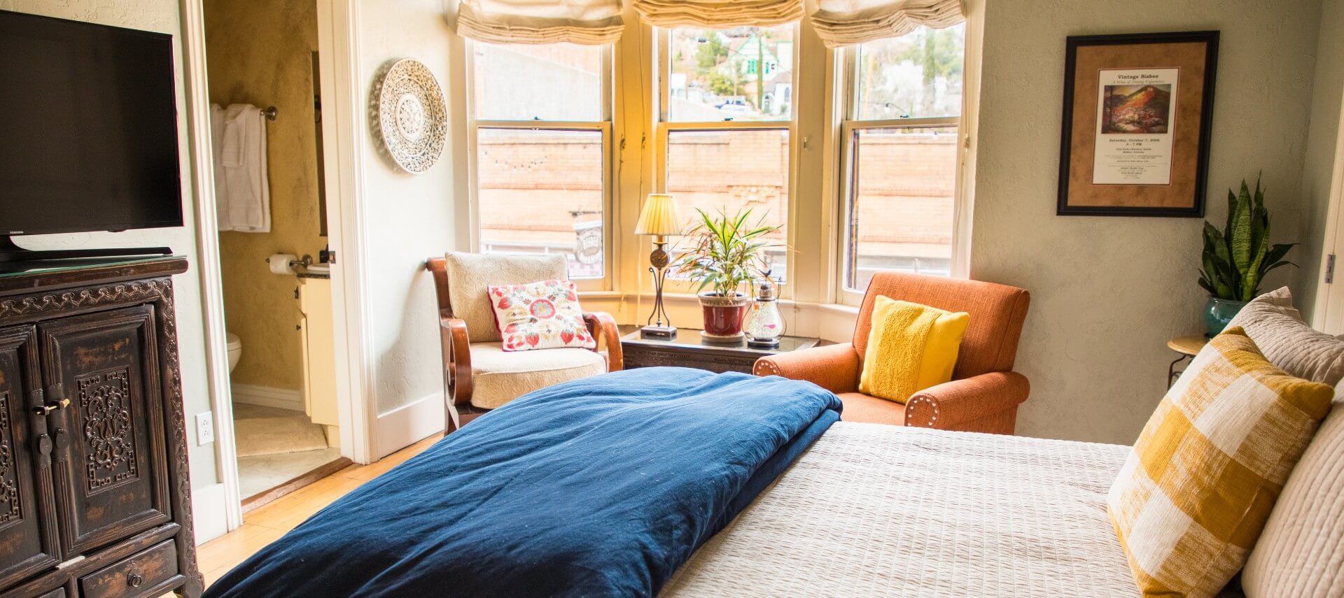 Luxurious suite with bed, orange sitting chairs, decorative armoire and doorway into bathroom