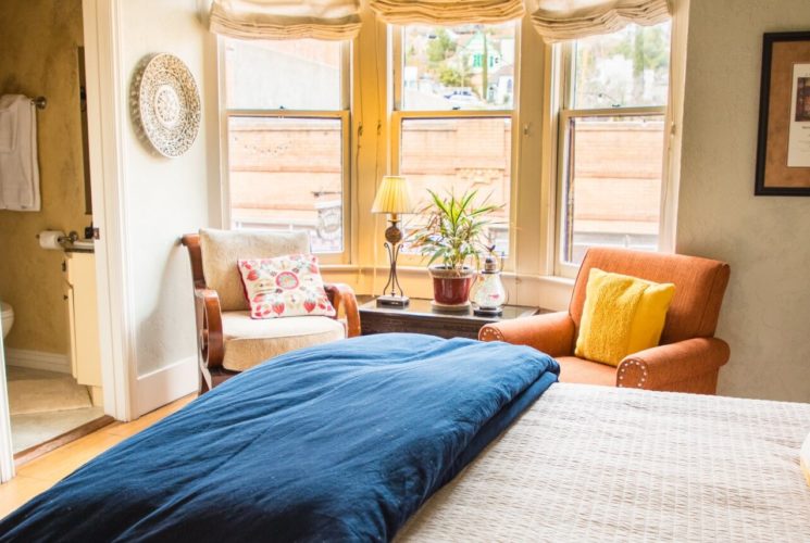 Luxurious suite with bed, orange sitting chairs, decorative armoire and doorway into bathroom