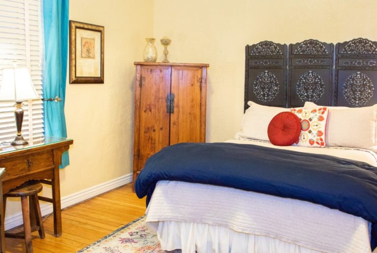 Queen bed with decorative headboard, corner armoire and desk in front of one window