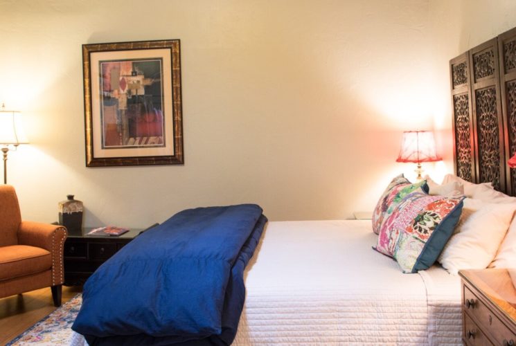 Queen bed and white and blue bedding decorative headboard, sitting chair, and closet with red curtain