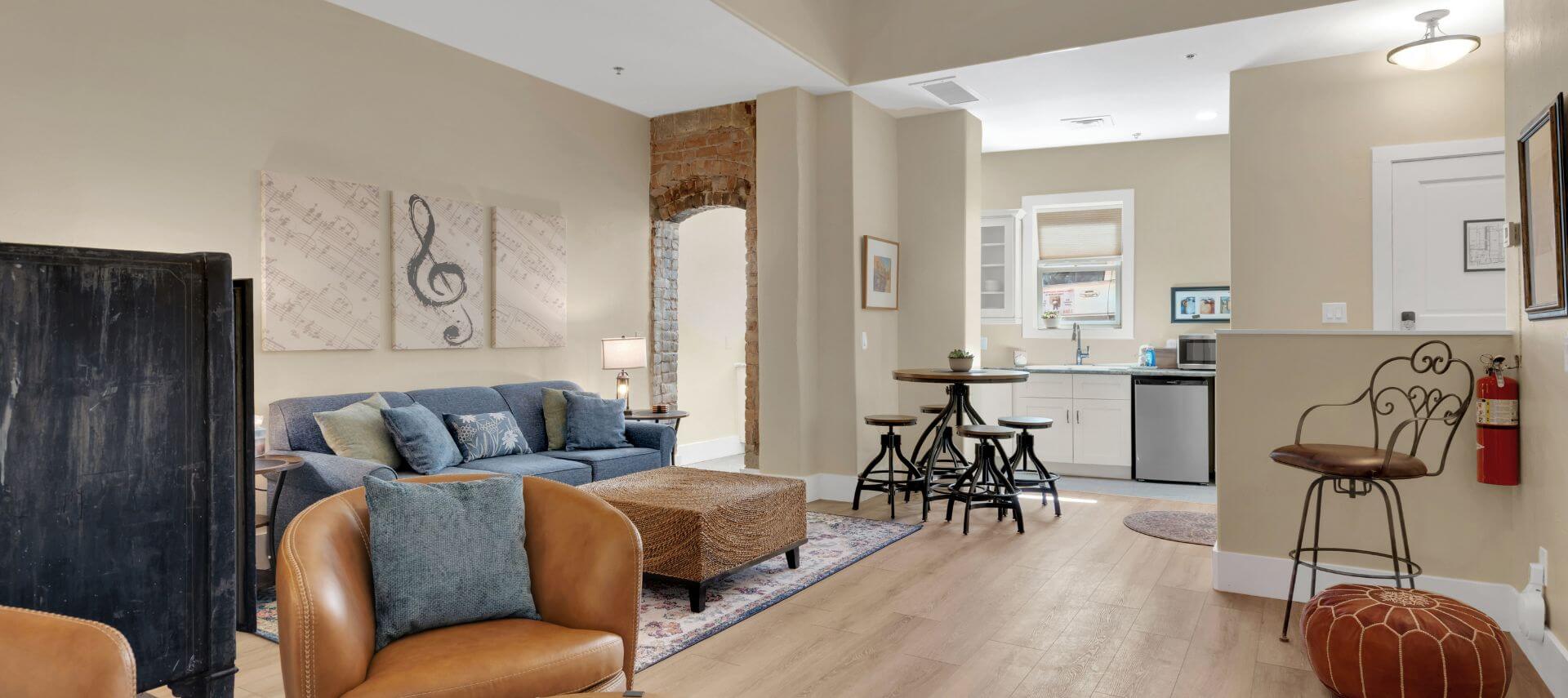 view of living room with blue couch, leather chairs, artwork on wall, kitchenette with round table and stools, narrow domed doorway opening