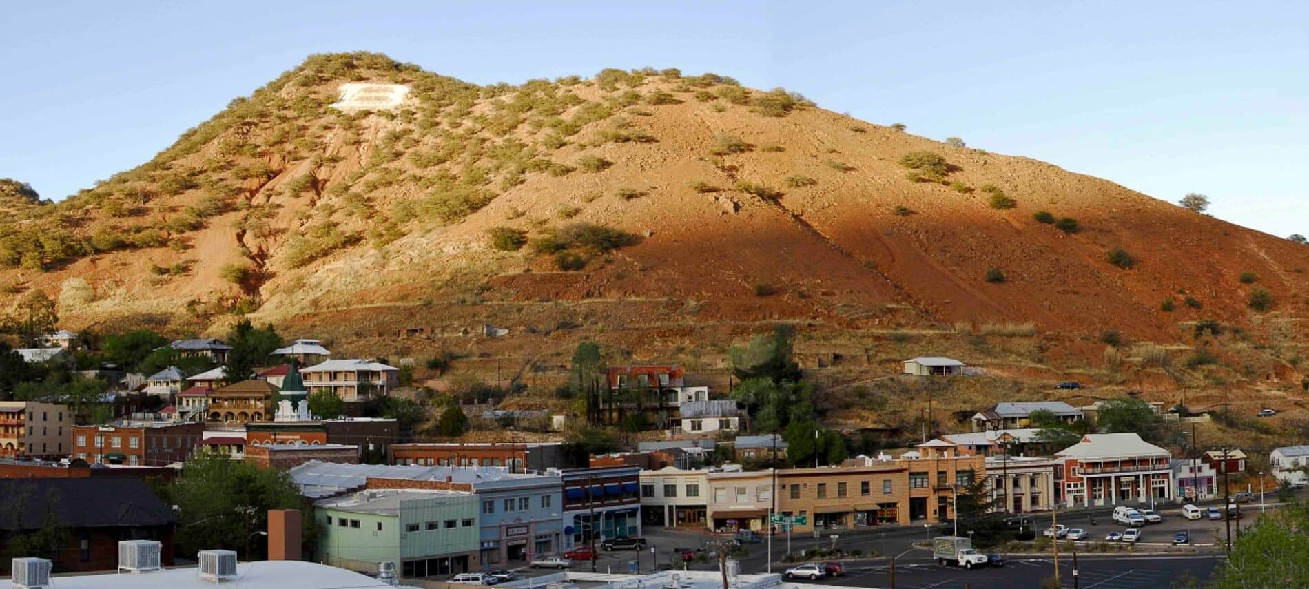 Single barren mountain with blue skies above and buildings of small town in valley below