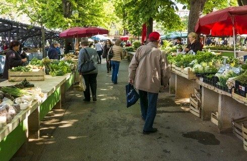 A farmer's market with various stands of vegetables and people walking