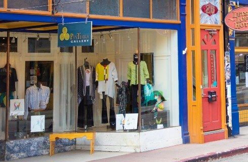 A storefront featuring colorful outfits through the window and a yellow bench out front