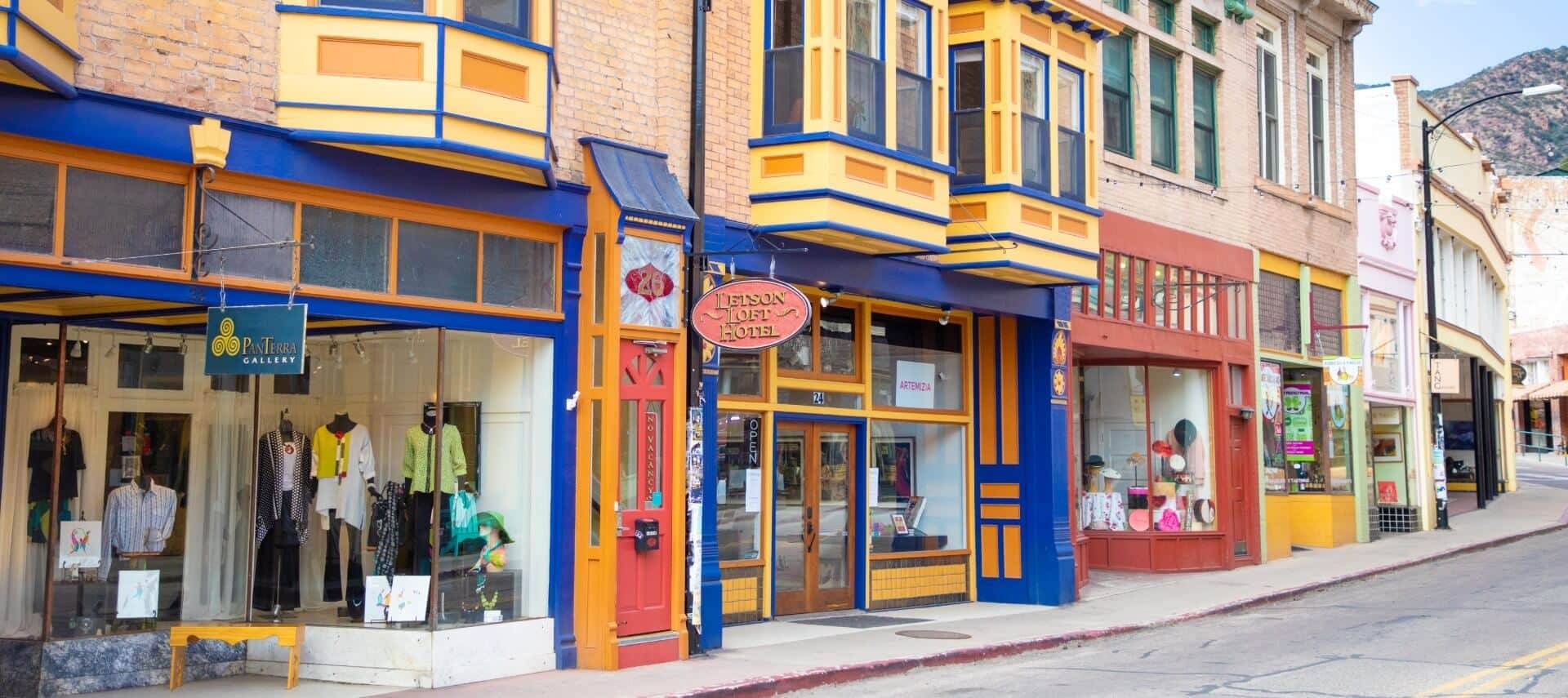 Empty street featuring several storefronts with different colors and a mountain range in the background