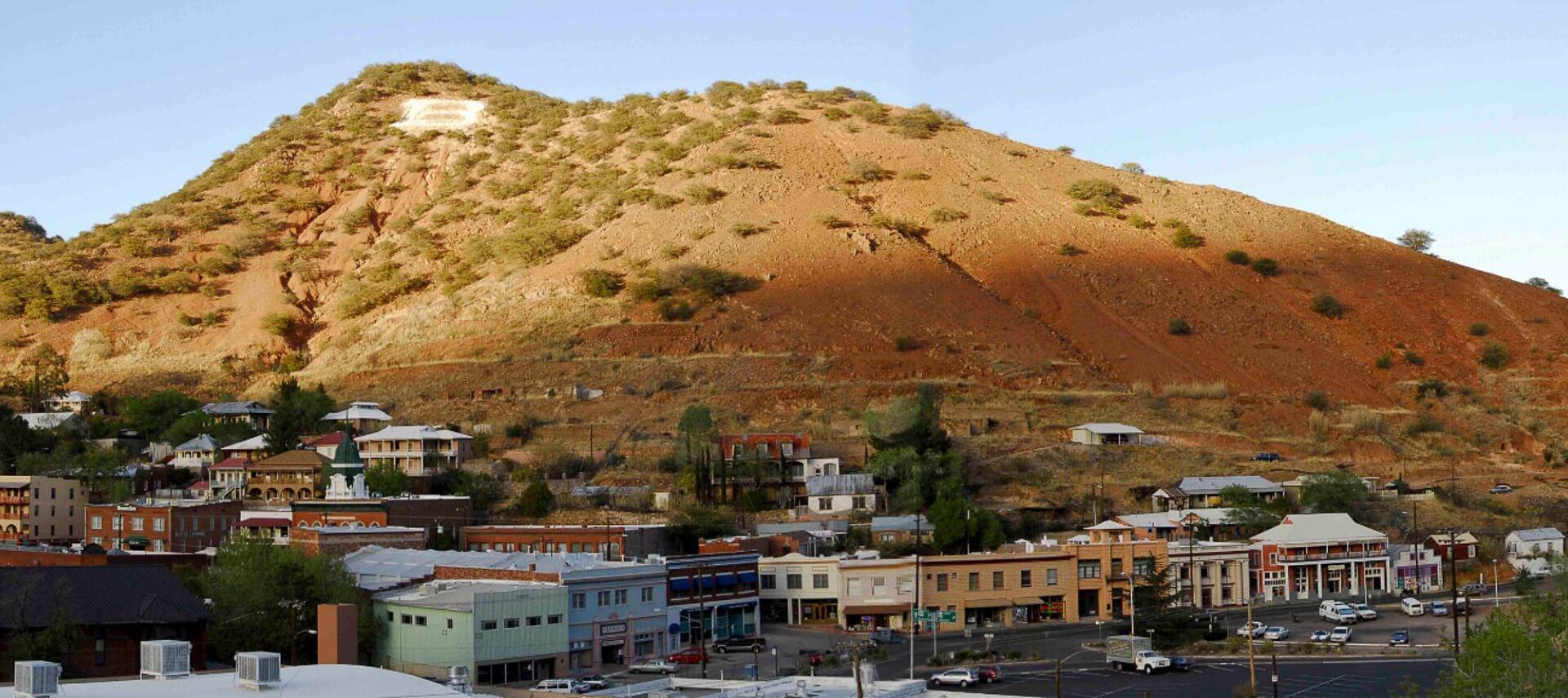 Tall single mountain range with few trees behind a small town with main street of buildings